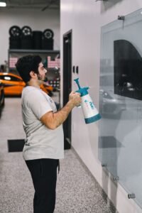 Man using a spray bottle to clean a glass surface in a modern garage setting.